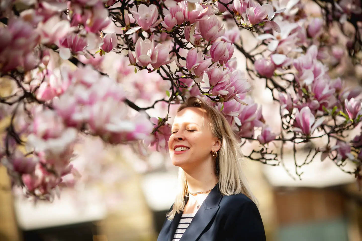 Svitlana Veselovska smiling with her eyes closed under a magnolia tree in bloom.